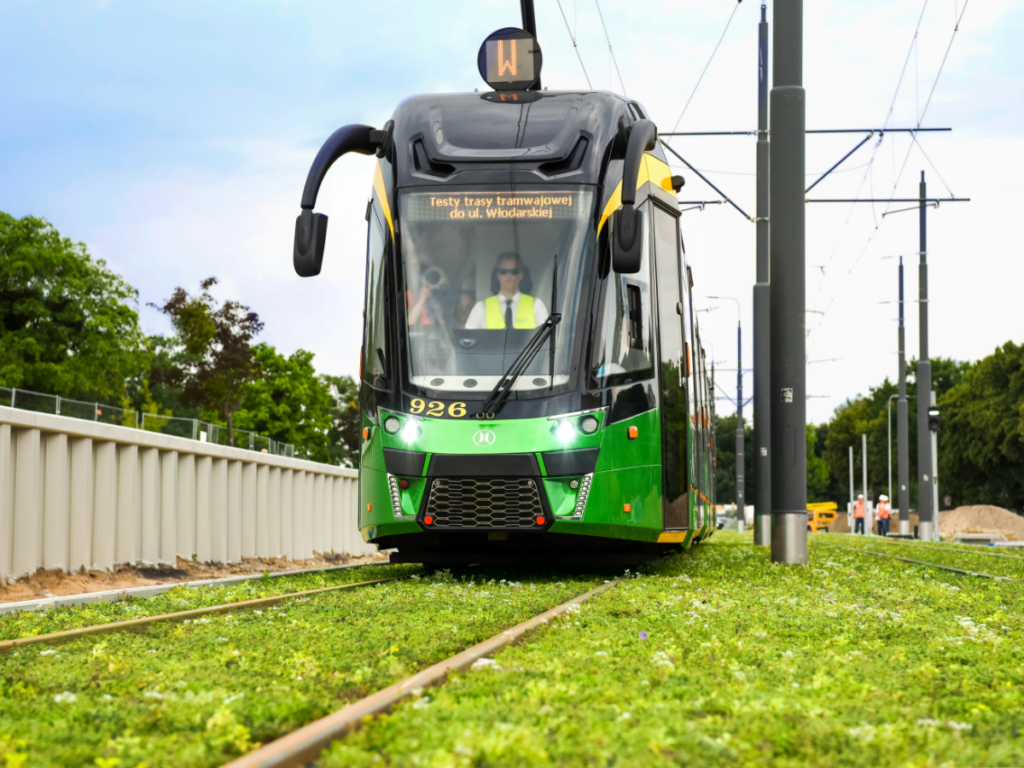 Tramwaj jadący po zielonych torach. Zdjęcie podglądowe